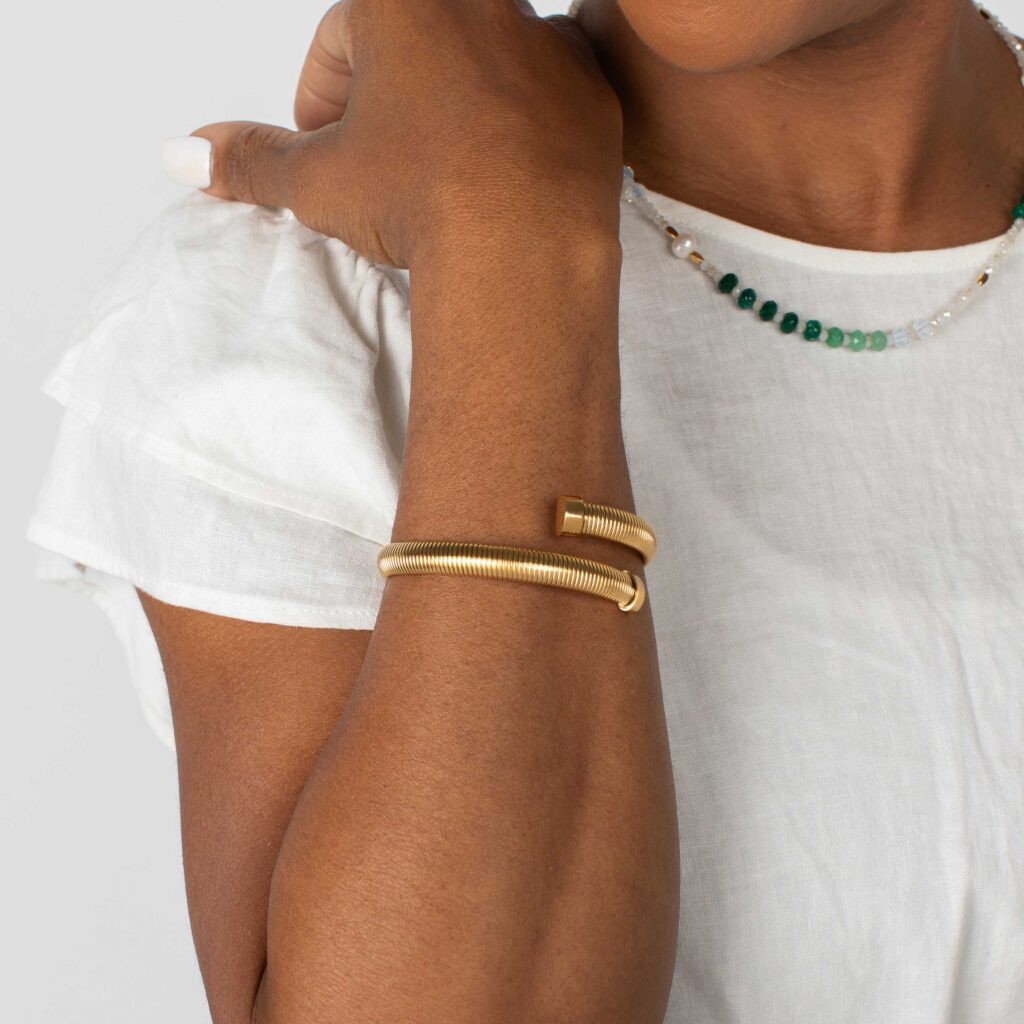 Gold Tamia Cuff Bracelet worn with a white ruffle-sleeved blouse and gemstone necklace.