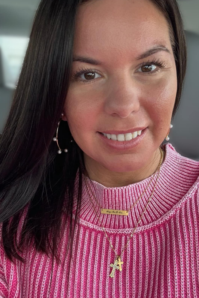 Smiling woman wearing gold hoop earrings adorned with small pearls, styled with layered gold necklaces and a pink ribbed sweater. Showcasing the JBloom Camellia Earrings in a casual, everyday look.