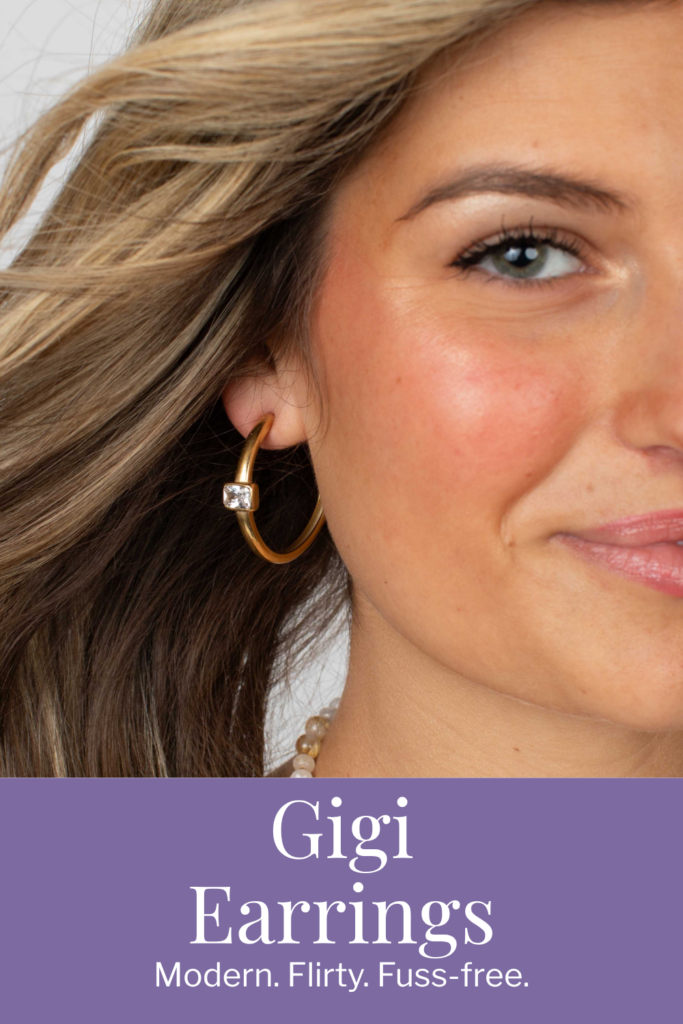 A close-up of a woman wearing the Gigi Earrings in stainless steel—mid-sized semi hoop earrings featuring a sleek crystal accent at the front.
A woman wears the Gigi Earrings in gold stainless with her hair softly flowing, showcasing the earrings’ modern hoop shape and subtle sparkle.