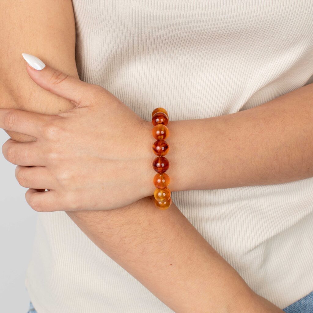 Close-up of a woman’s wrist wearing a burnt-orange marbled resin bead bracelet, styled with a cream ribbed top.